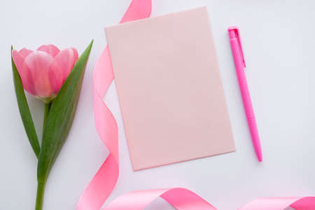 top view of ribbon and envelope near pink tulip on whiteの写真素材