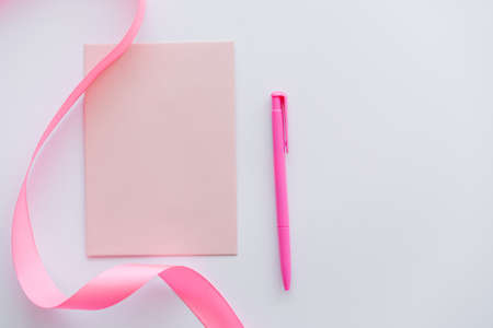 top view of pen near envelope and pink ribbon on whiteの写真素材