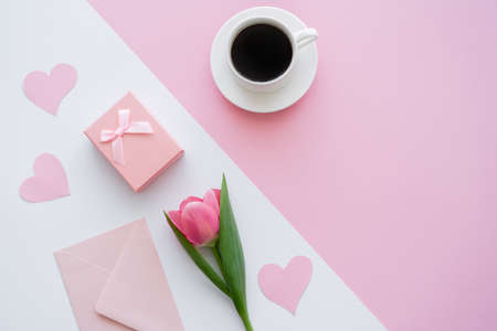 top view of envelope near cup with coffee, gift box and tulip on white and pinkの写真素材
