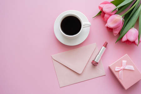 top view of blooming tulips near lipstick, envelope and cup of coffee on pinkの写真素材
