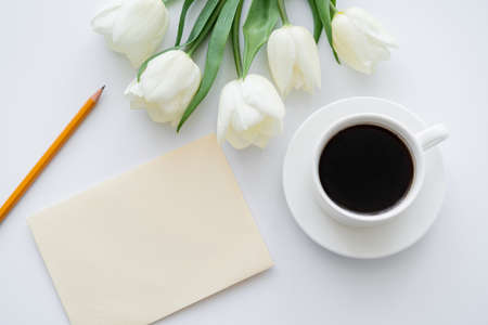 top view of envelope with pencil near cup with coffee and tulips on whiteの写真素材