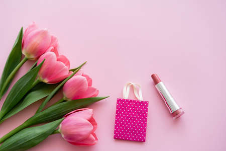 top view of blooming tulips near lipstick and small shopping bag on pinkの写真素材