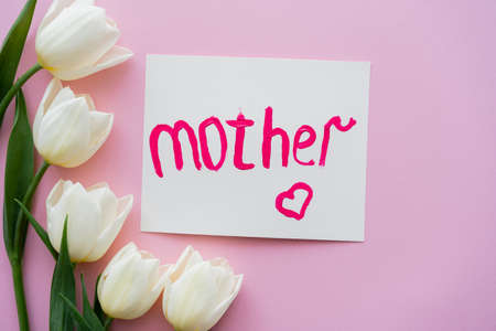 top view of white tulips near greeting card with mother lettering on pinkの写真素材