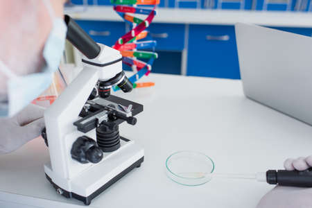 partial view of blurred geneticist holding micropipette near petri dish while working with...