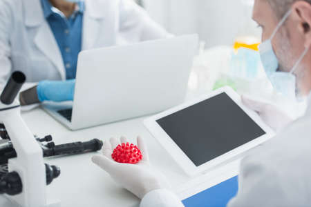 biologist in medical mask holding digital tablet with blank screen and coronavirus bacteria model