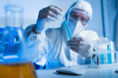 blurred scientist in hazmat suit holding test tube in chemical laboratory