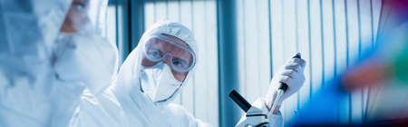 scientist in goggles and medical mask near microscope and colleague on blurred foreground, bannerの写真素材