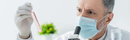 mature scientist in medical mask holding test tube with liquid, banner