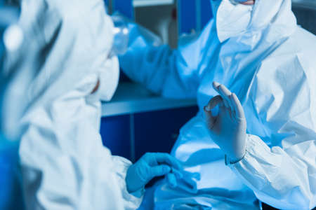 cropped view of virologist in hazmat suit and latex gloves showing okay gesture near colleague