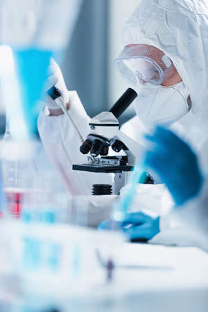 bioengineer in hazmat suit working with microscope on blurred foreground