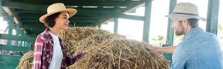 interracial farmers smiling at each other near haystack on farm, banner