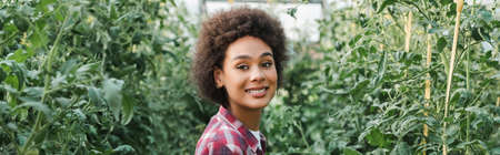 young african american woman smiling at camera in plant nursery, banner