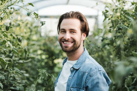 young brunette farmer smiling at camera in greenhouseの写真素材