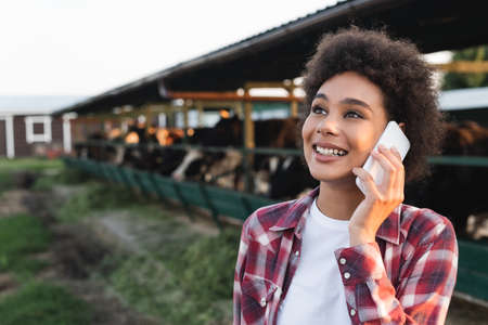 cheerful african american woman looking away while talking on smartphone on farm