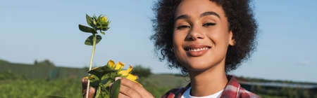 happy african american farmer looking at camera near sunflowers in field, bannerの写真素材