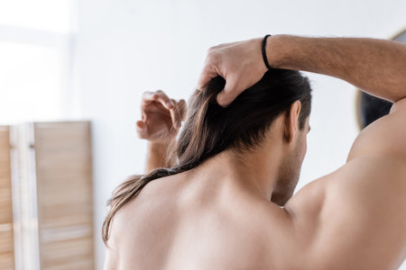 back view of shirtless man styling long hair in bathroomの写真素材