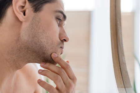 close up view of man touching chin while looking at mirror