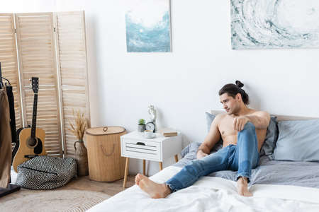barefoot man in jeans resting on bed at homeの写真素材