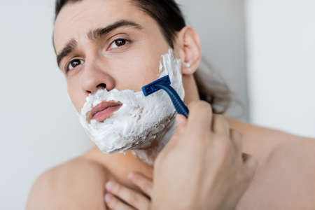shirtless man with foam on face shaving in bathroomの写真素材