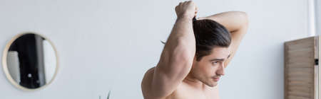 muscular man adjusting long hair while standing in modern bathroom, bannerの写真素材