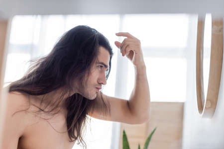 side view of shirtless man styling long hair near mirrorの写真素材