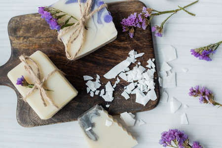 Top view of homemade soap near flakes on cutting board and flowers on tableの写真素材
