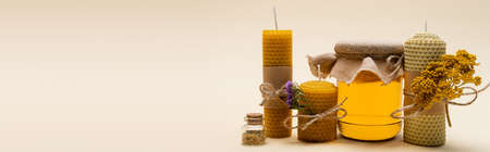 Craft candles with flowers near jar with honey on beige background, bannerの写真素材