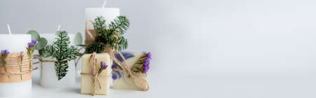 Handmade soap with flowers near candles with pine branches on grey background, bannerの写真素材
