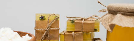 Close up view of handmade soap bars and flakes near honey isolated on grey, bannerの写真素材