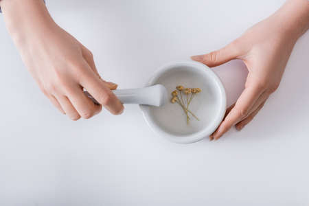 top view of woman grinding dried flowers in mortar with pestle on whiteの写真素材