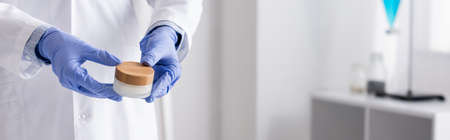 cropped view of chemist in latex gloves holding container with cream, bannerの写真素材