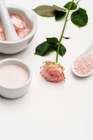 flower near pink sea salt, bowl with cream, pestle and mortar with petals on whiteの写真素材
