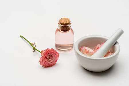 flower near pestle and mortar with petals and bottle with rose water on whiteの写真素材