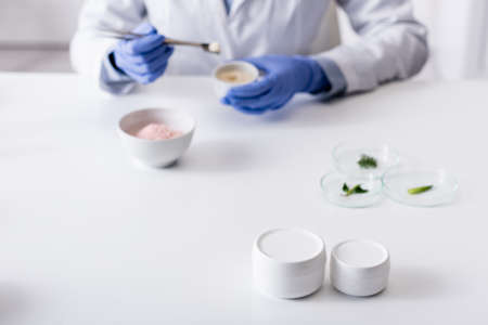 containers with cream near blurred laboratory assistant in latex gloves