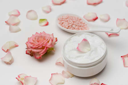 flower near petals, pink sea salt and container with cream on whiteの写真素材