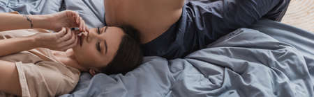 Young woman in t-shirt lying near shirtless boyfriend on bed, bannerの写真素材