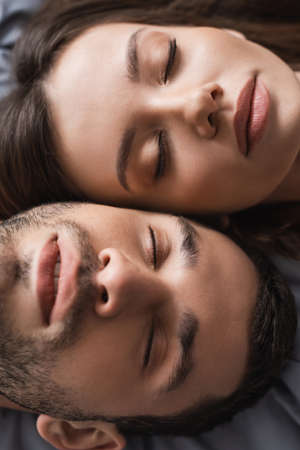 Top view of young couple with closed eyes lying on bedの写真素材