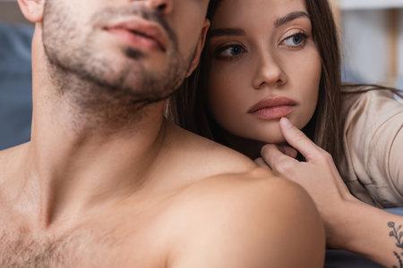 Pretty woman touching chin near shirtless boyfriend at homeの写真素材