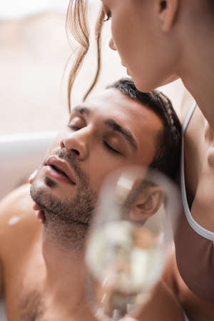 Woman holding blurred champagne and looking at bearded boyfriend in bathtubの写真素材