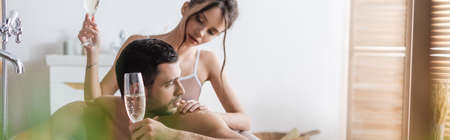 Pretty woman touching muscular man with glass of champagne in bathtub, bannerの写真素材