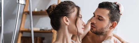 Brunette woman in foam hugging shirtless boyfriend in bathroom, banner