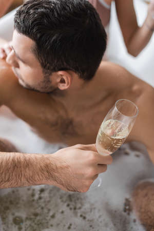 Overhead view of young man holding glass of champagne near blurred girlfriend in bathtubの写真素材
