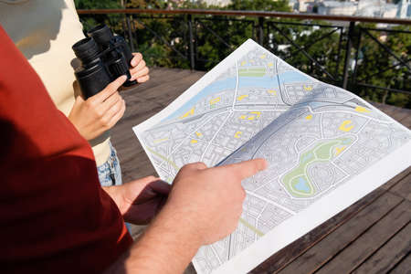 Cropped view of tourist pointing at map near girlfriend with binoculars outdoorsの写真素材