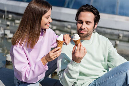 Smiling woman holding ice cream near boyfriend on urban streetの写真素材