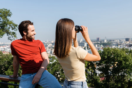 Positive man looking away near girlfriend with binoculars in cityの写真素材