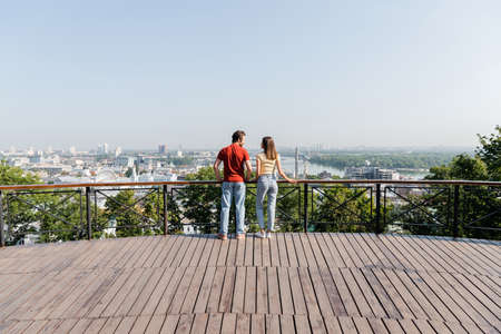 Side view of positive tourists looking at each other on viewpoint in city