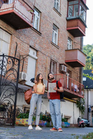 Young couple with map and binoculars looking away near building on urban streetの写真素材