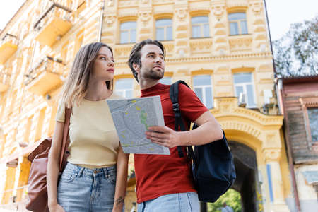 Low angle view of travelers with backpacks and map looking away on urban street
