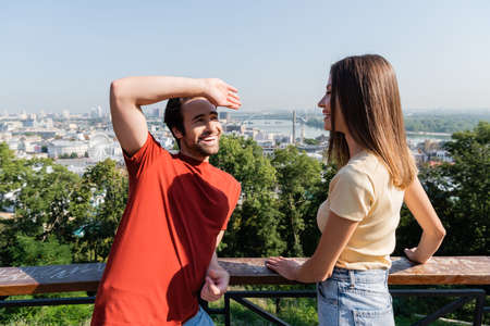 Happy man looking at girlfriend near railing on viewpoint in city