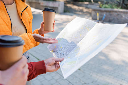Cropped view of tourist pointing at map near boyfriend with coffee to go on urban street